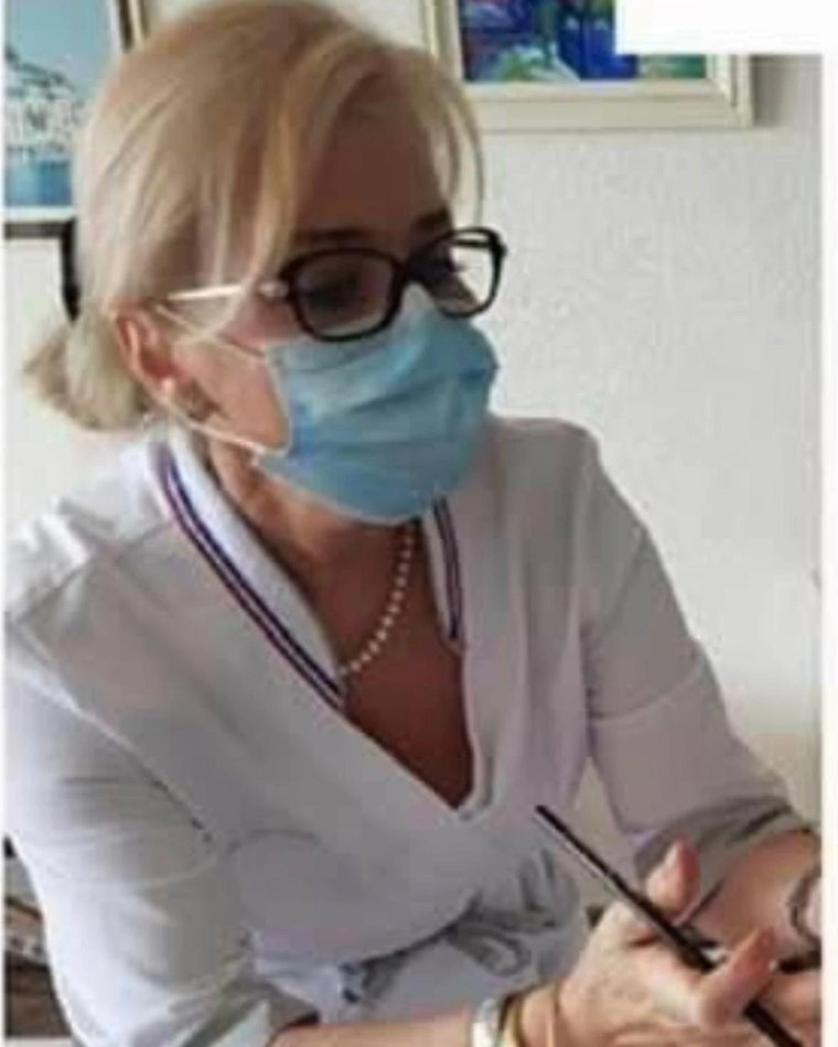 Sabine Comble, masquée et en blouse au col tricolore, réalise un maquillage permanent